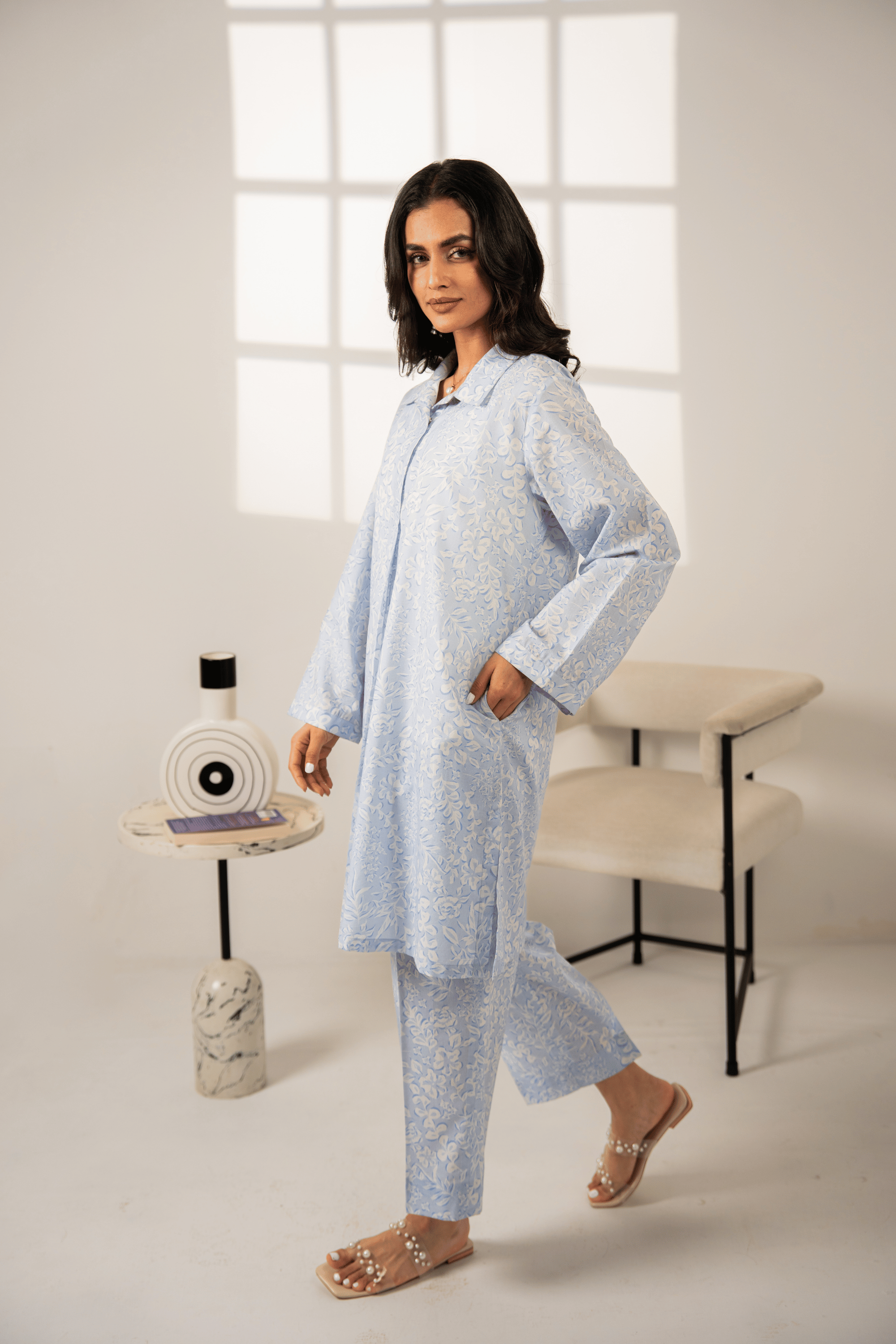 Woman wearing a light blue pajama set in a minimalistic room.