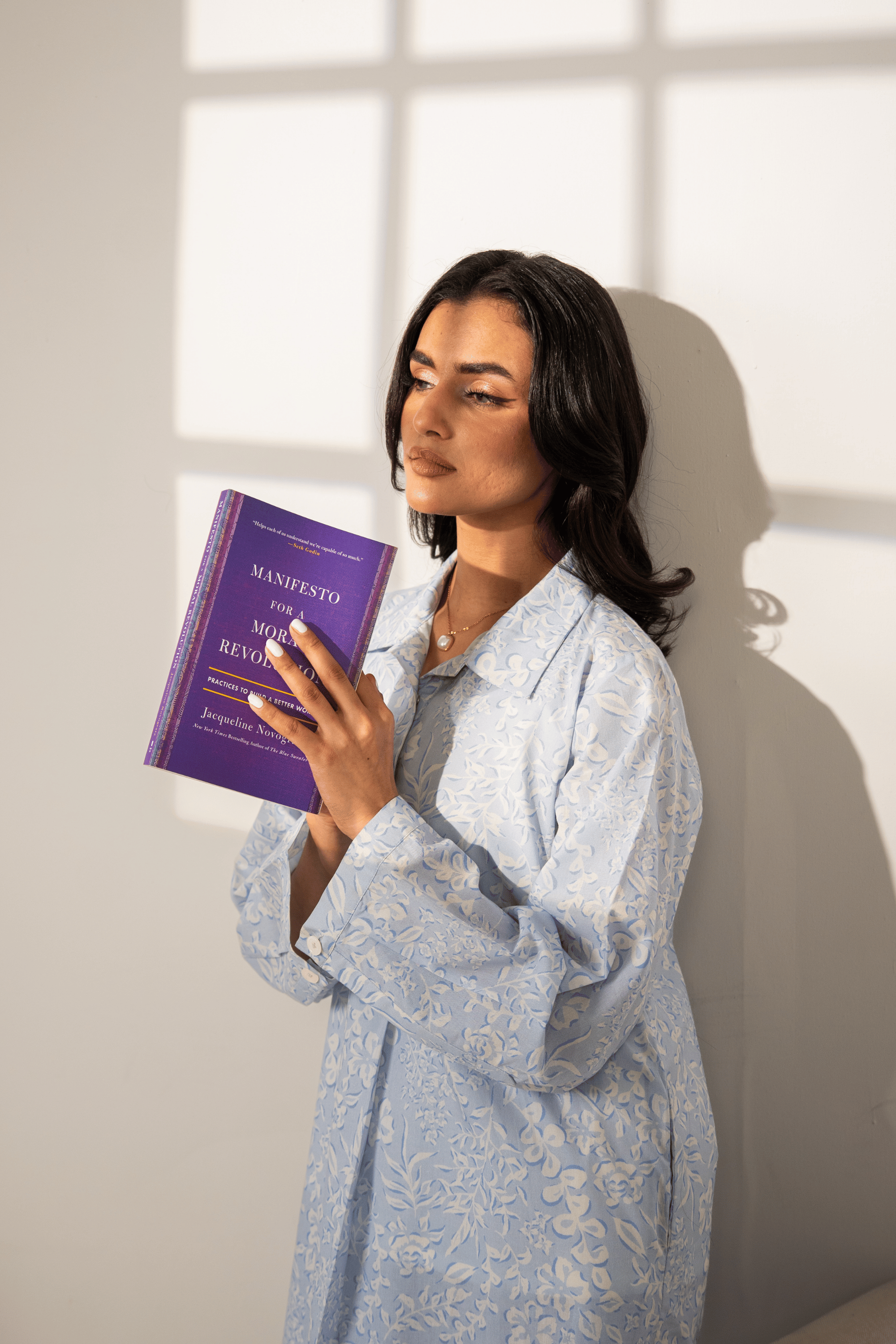 Woman holding a purple book titled 'Manifiesto' by Manuela Revuelta against a light background
